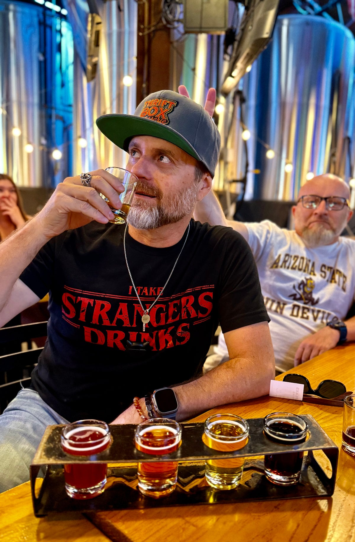 Man drinking beer while his friend makes a victory sign with his fingers behind him
