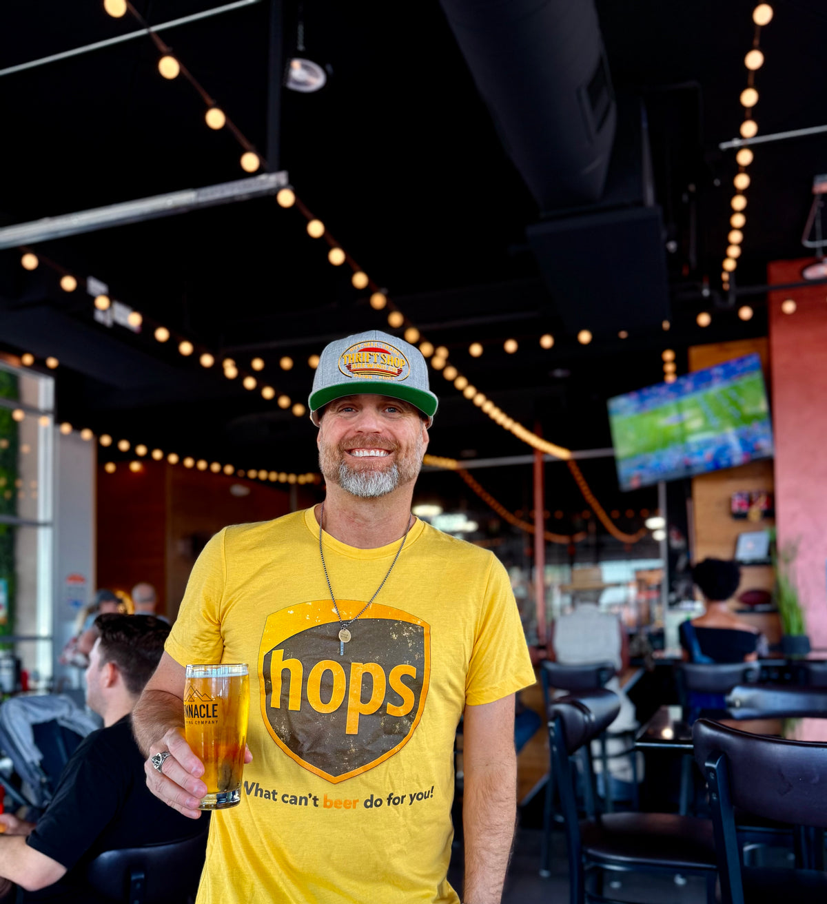 Smiling man holding a beer mug while wearing a Brewtiful Adventures T-shirt and hat